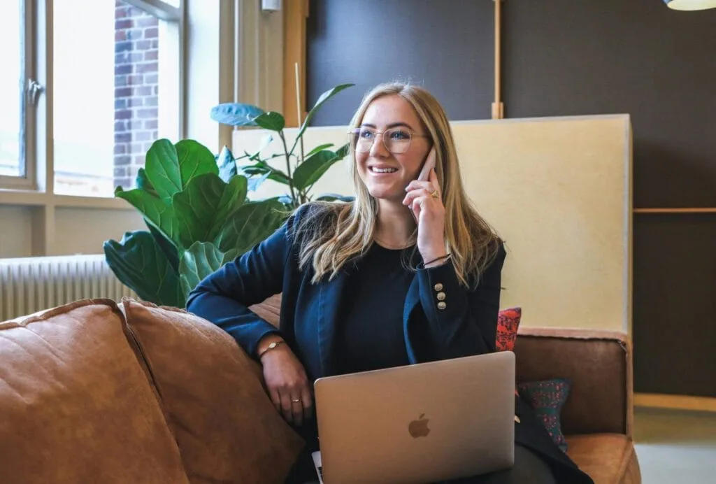 Lady on her cell phone with laptop smiling.