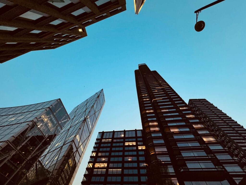 Low-angle view of modern skyscrapers and office buildings against a clear blue evening sky.