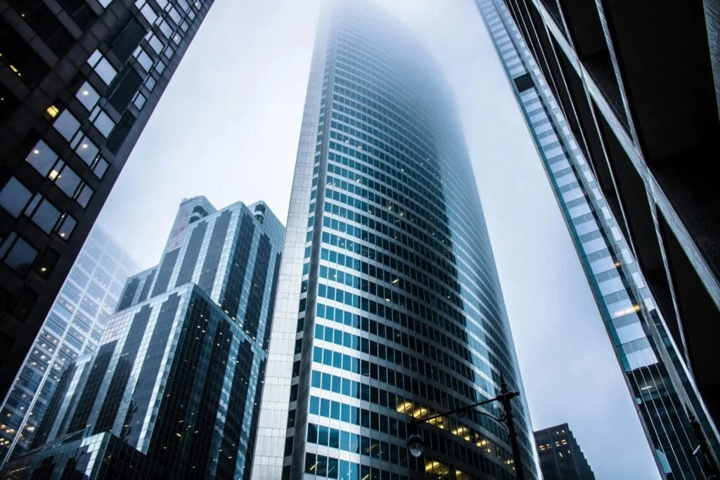Low-angle view of modern skyscrapers with a tall building disappearing into the foggy sky.